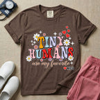 A t-shirt featuring the text Tiny Humans are my favorite in colorful retro bubble letters decorated with daisies, sparkles, and red hearts with a small NICU heart logo at the bottom.