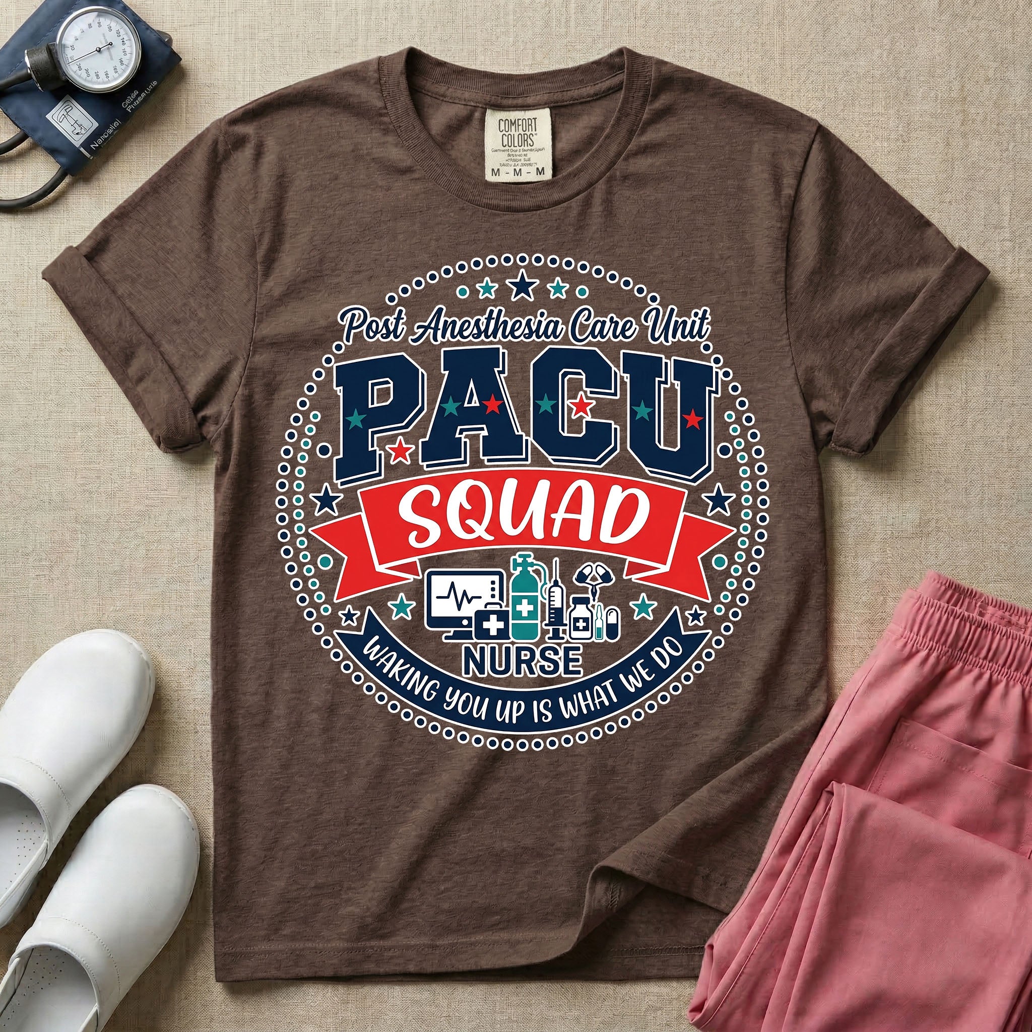 A t-shirt featuring a circular badge design with the text PACU SQUAD in block letters, medical icons like a heart monitor and stethoscope, and the phrase Waking You Up Is What We Do.