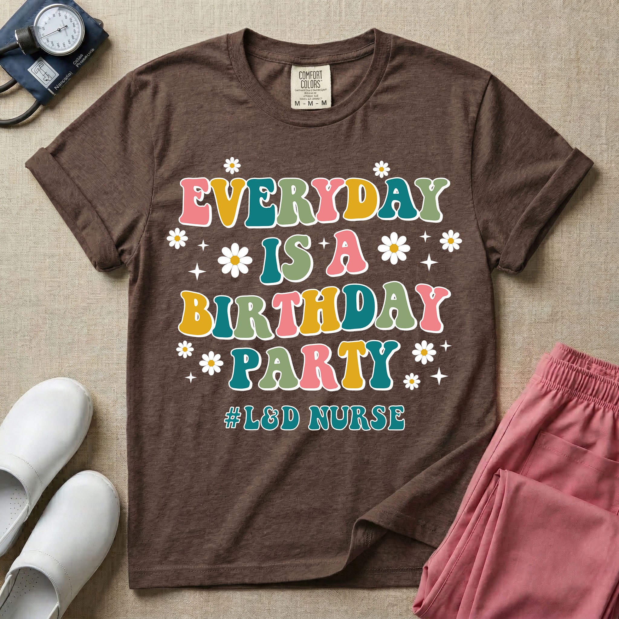 A retro graphic tee for labor and delivery nurses featuring bubble lettering that reads "EVERYDAY IS A BIRTHDAY PARTY #L&D NURSE" surrounded by small daisies and stars.