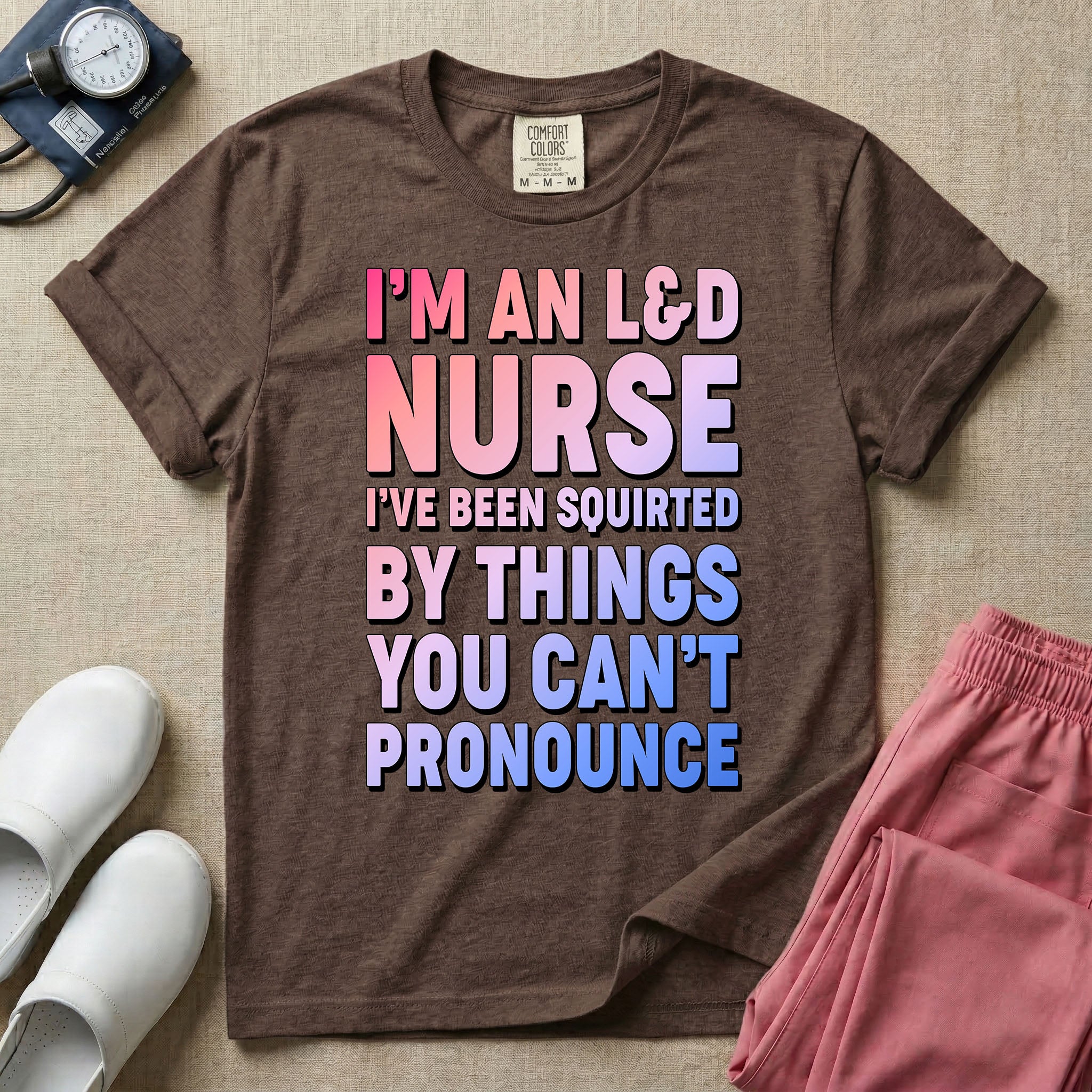 A humorous graphic tee for labor and delivery nurses featuring bold, gradient block lettering that reads "I'M AN L&D NURSE I'VE BEEN SQUIRTED BY THINGS YOU CAN'T PRONOUNCE".