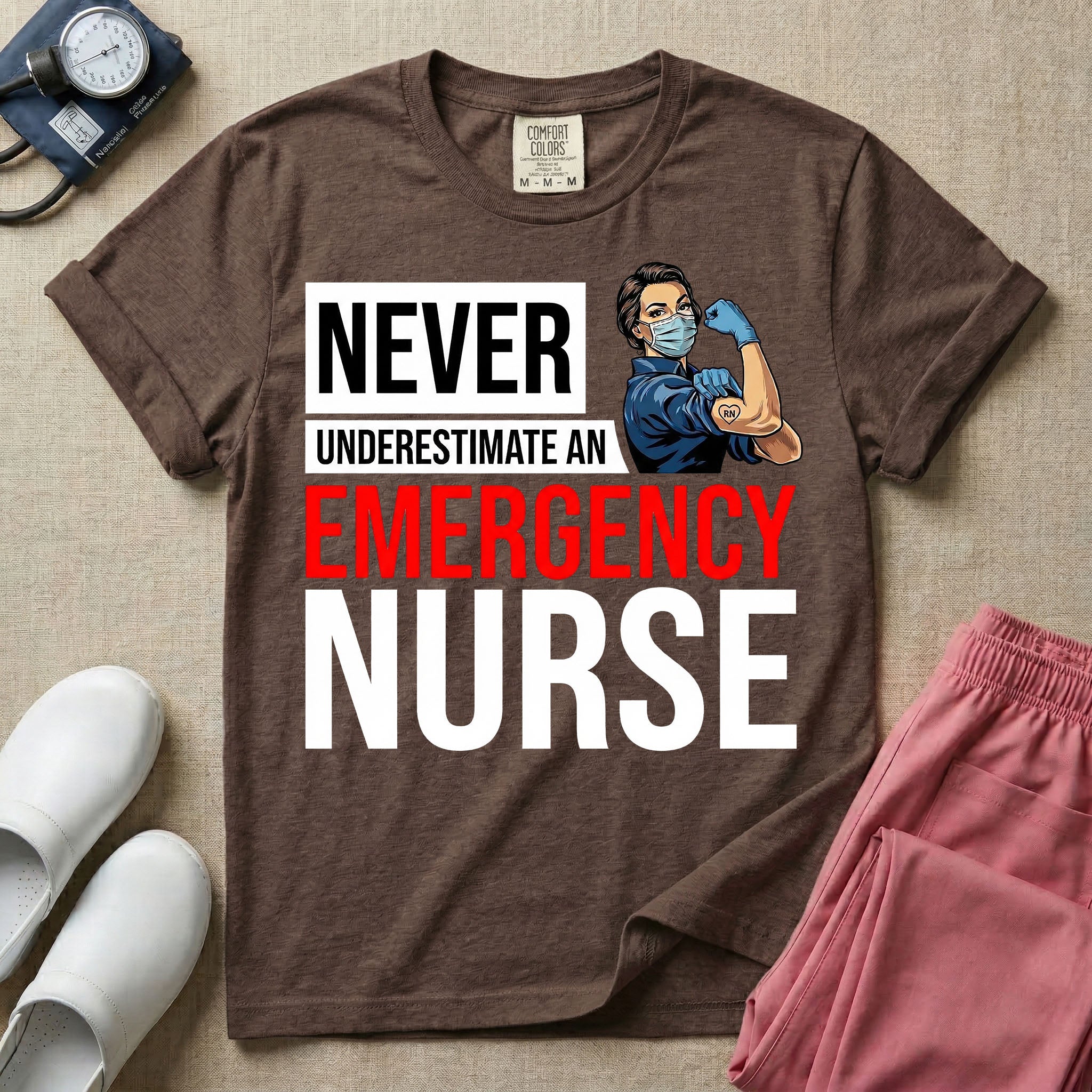 A retro ER nursing t-shirt featuring the bold text "NEVER UNDERESTIMATE AN EMERGENCY NURSE" alongside a vintage graphic of a masked nurse flexing her arm in a classic Rosie the Riveter pose