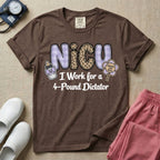 A funny t-shirt for NICU nurses featuring the text "NICU I Work for a 4-Pound Dictator" designed with purple plaid and leopard print letters, accompanied by graphics of a baby bottle with a bow and a rattle that says "WARNING: TINY BOSS".