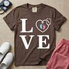A minimalist nursing t-shirt featuring the word LOVE stacked in large white serif letters, with the letter O replaced by a white stethoscope shaped like a heart containing two small baby footprints, one pink and one blue.