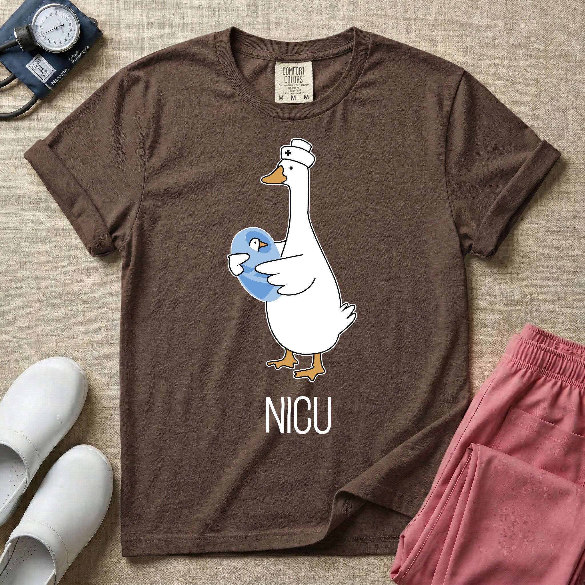 A t-shirt featuring an illustration of a white silly goose wearing a nurse's cap and holding a baby goose swaddled in a blue blanket, with the text NICU printed below.