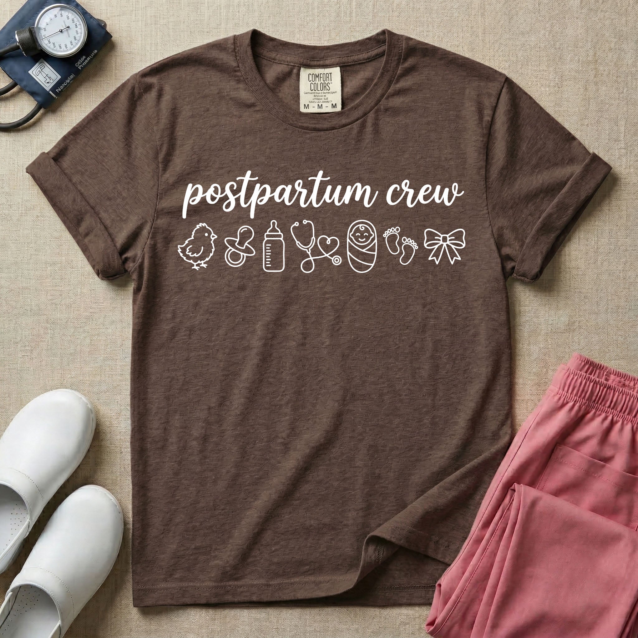 A t-shirt featuring the lowercase text postpartum crew in a cursive script font above a horizontal row of minimalist line-art icons including a baby chick, a pacifier, a baby bottle, a heart-shaped stethoscope, a swaddled baby, baby footprints, and a ribbon bow.