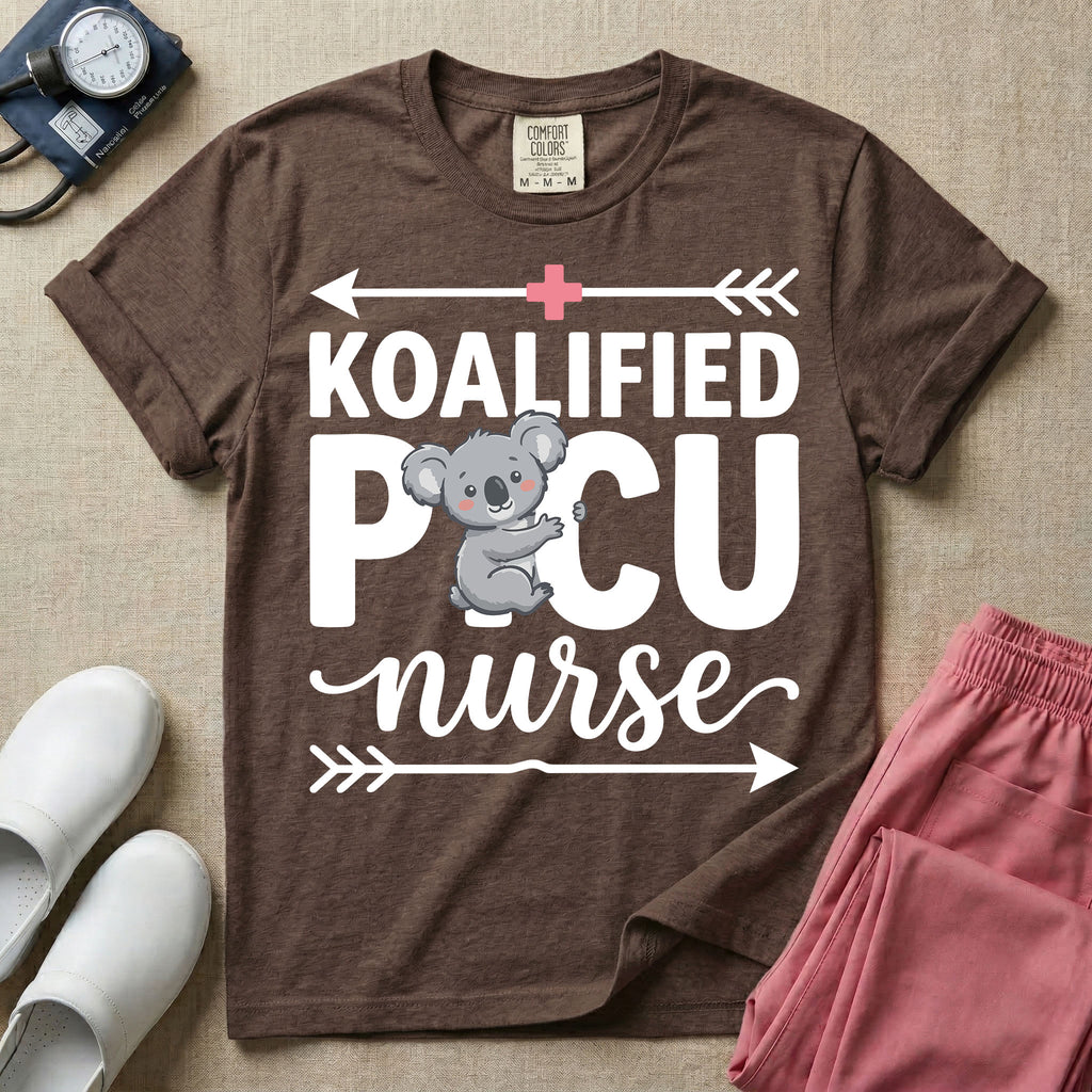 A funny pediatric intensive care nursing t-shirt featuring the pun text "KOALIFIED PICU nurse" with a cute koala graphic replacing the letter I in PICU, framed by decorative arrows and a pink medical cross.
