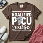 A funny pediatric intensive care nursing t-shirt featuring the pun text "KOALIFIED PICU nurse" with a cute koala graphic replacing the letter I in PICU, framed by decorative arrows and a pink medical cross.