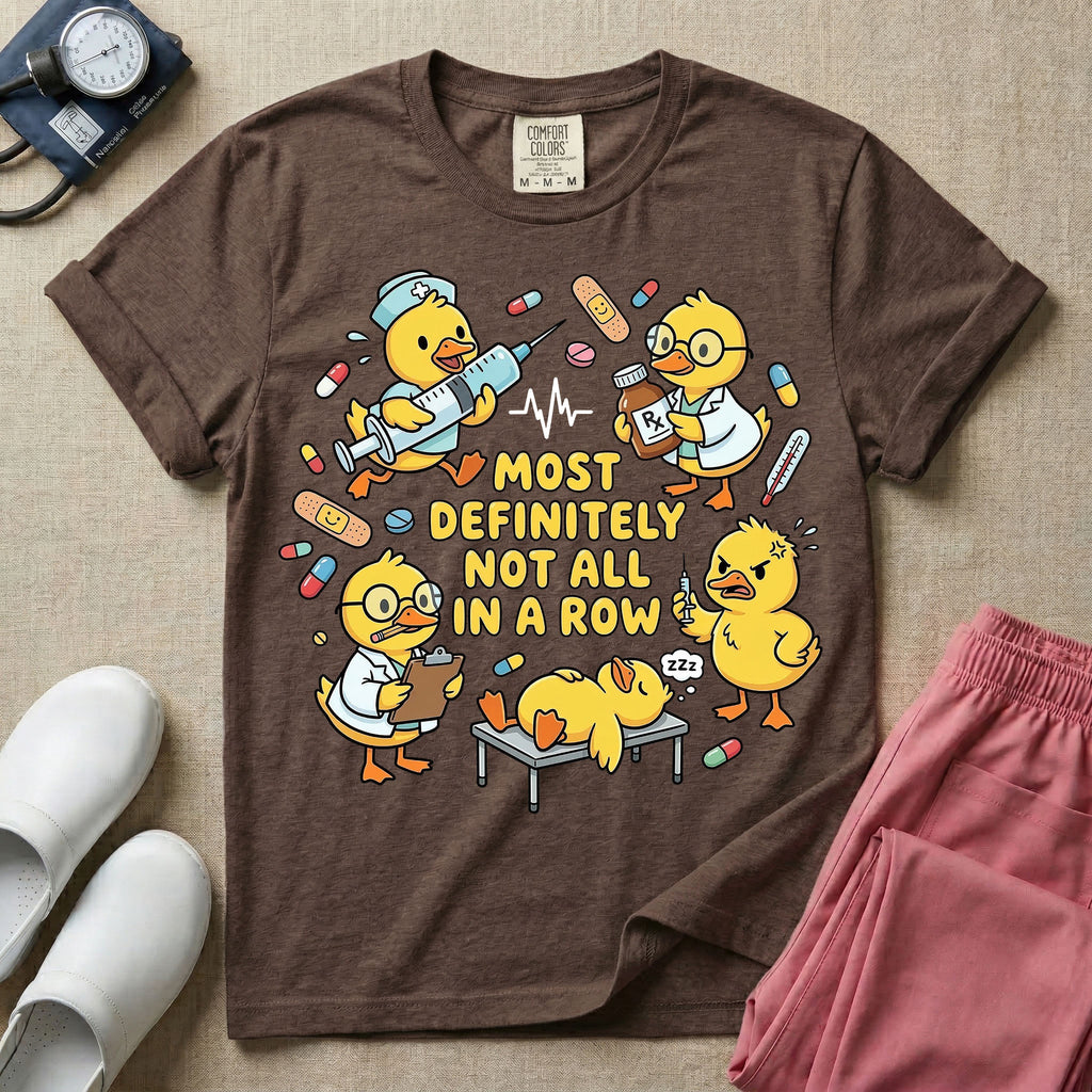 General nursing t-shirt featuring a chaotic group of cartoon ducklings dressed as medical professionals with the text "MOST DEFINITELY NOT ALL IN A ROW" on a sage green garment, in espresso color.