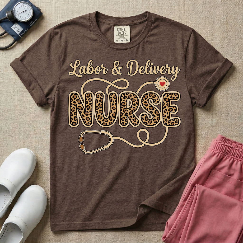 A graphic t-shirt for a Labor and Delivery unit featuring the text 'Labor & Delivery' in beige script above the word 'NURSE' in large leopard print letters, intertwined with an illustration of a stethoscope that features a small red heart on the chest piece.