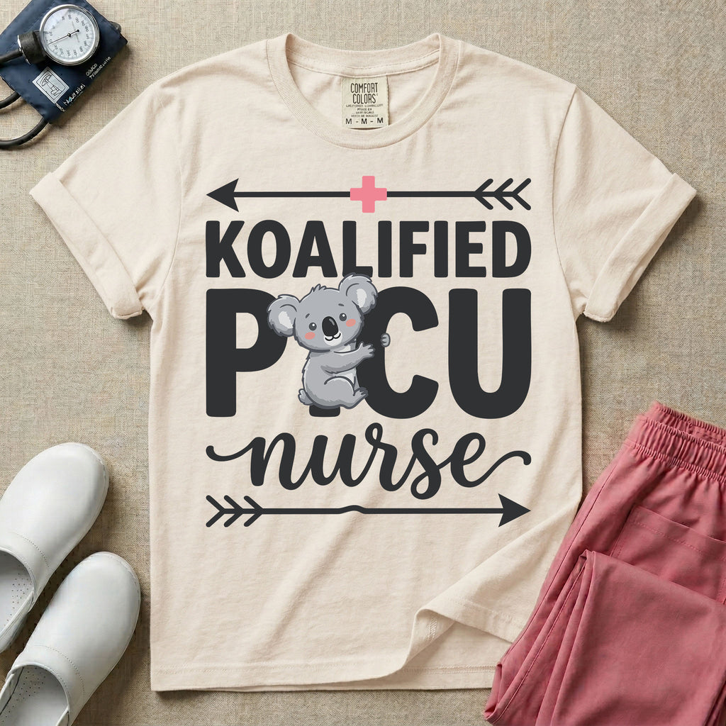 A funny pediatric intensive care nursing t-shirt featuring the pun text "KOALIFIED PICU nurse" with a cute koala graphic replacing the letter I in PICU, framed by decorative arrows and a pink medical cross.