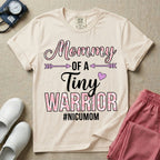 A cute NICU mom t-shirt featuring the stacked text "Mommy OF A Tiny WARRIOR #NICUMOM" in pink and white, accented with decorative arrows, a small pink heart, and a pink plaid pattern filling the word warrior.