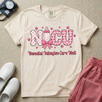 Retro coquette style t-shirt graphic featuring decorative pink 'NICU' text with checkerboard and heart patterns, incorporating a baby bottle with a bow and hearts, and the cursive text 'Neonatal Intensive Care Unit' below.