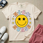 A t-shirt featuring a large yellow smiley face with star eyes surrounded by smiley face daisies and the text N.I.C.U. NURSE in pastel retro bubble lettering.