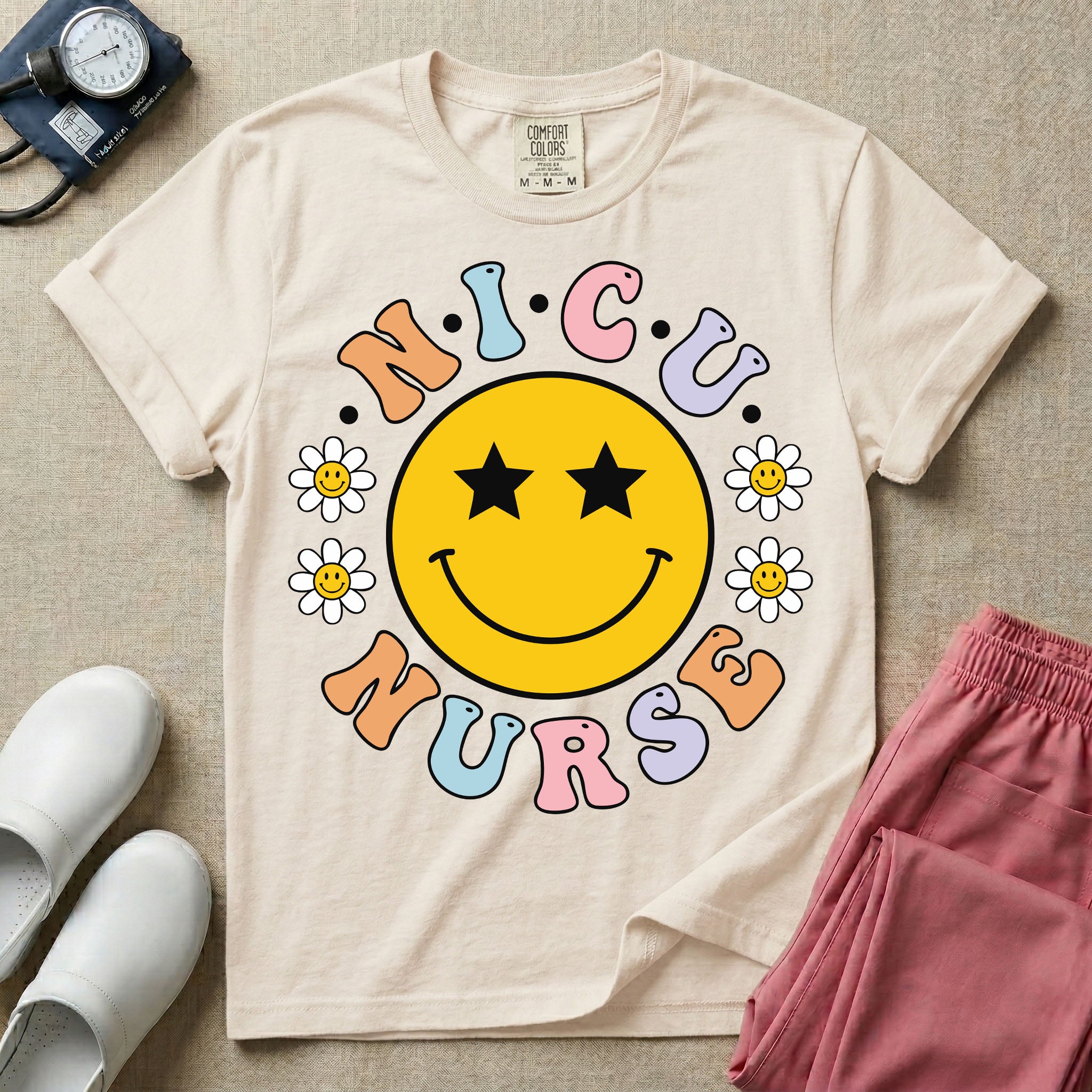 A t-shirt featuring a large yellow smiley face with star eyes surrounded by smiley face daisies and the text N.I.C.U. NURSE in pastel retro bubble lettering.