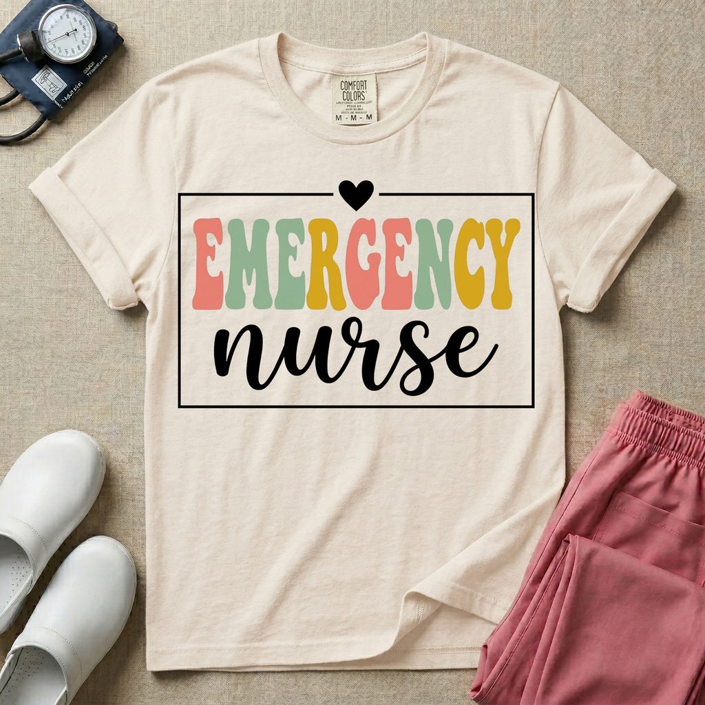 A retro-style t-shirt for emergency room nurses featuring the word "EMERGENCY" in colorful, vintage lettering above the word "nurse" in a delicate white script font, framed by a thin white rectangular border with a small heart at the top center.