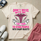General nursing and ER t-shirt featuring a pink and black caduceus medical symbol flanked by two syringes alongside the humorous text "DON'T MESS WITH ME... I GET PAID TO STAB PEOPLE WITH SHARP OBJECTS".
