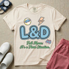A humorous Labor and Delivery nurse graphic featuring large, light blue varsity-style letters spelling L&D with a pink dashed outline, surrounded by small patch-like icons of a baby and a lightning bolt, sitting above cursive text that reads Full Moon: It's a Fluid Situation.