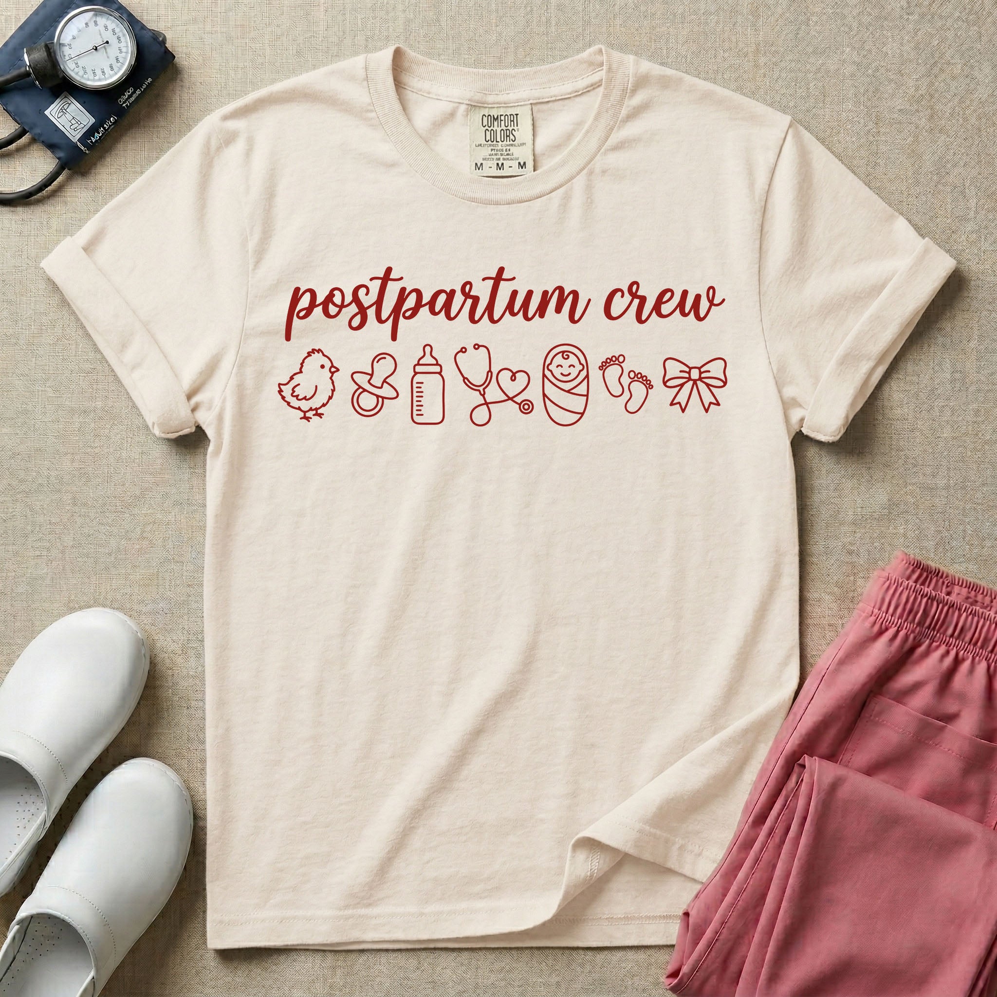 A t-shirt featuring the lowercase text postpartum crew in a cursive script font above a horizontal row of minimalist line-art icons including a baby chick, a pacifier, a baby bottle, a heart-shaped stethoscope, a swaddled baby, baby footprints, and a ribbon bow.