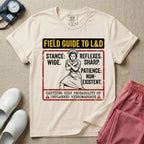 A humorous and retro graphic tee for labor and delivery nurses featuring a vintage nurse illustration alongside the text "FIELD GUIDE TO L&D", "STANCE: WIDE", "REFLEXES: SHARP", "PATIENCE: NON-EXISTENT", and "CAUTION: HIGH PROBABILITY OF UNPLANNED HYDROMASSAGE".