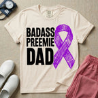 A graphic for the Neonatal Intensive Care Unit featuring the stacked, bold white text 'BADASS PREEMIE DAD' next to a large, textured purple awareness ribbon.