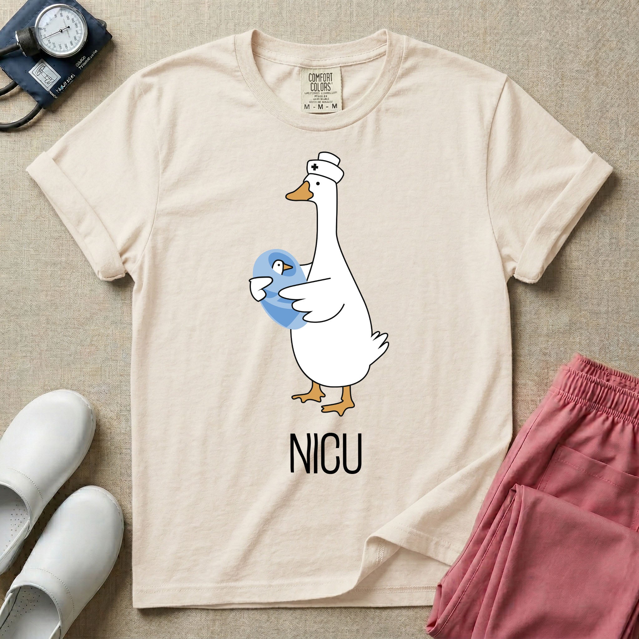 A t-shirt featuring an illustration of a white silly goose wearing a nurse's cap and holding a baby goose swaddled in a blue blanket, with the text NICU printed below.