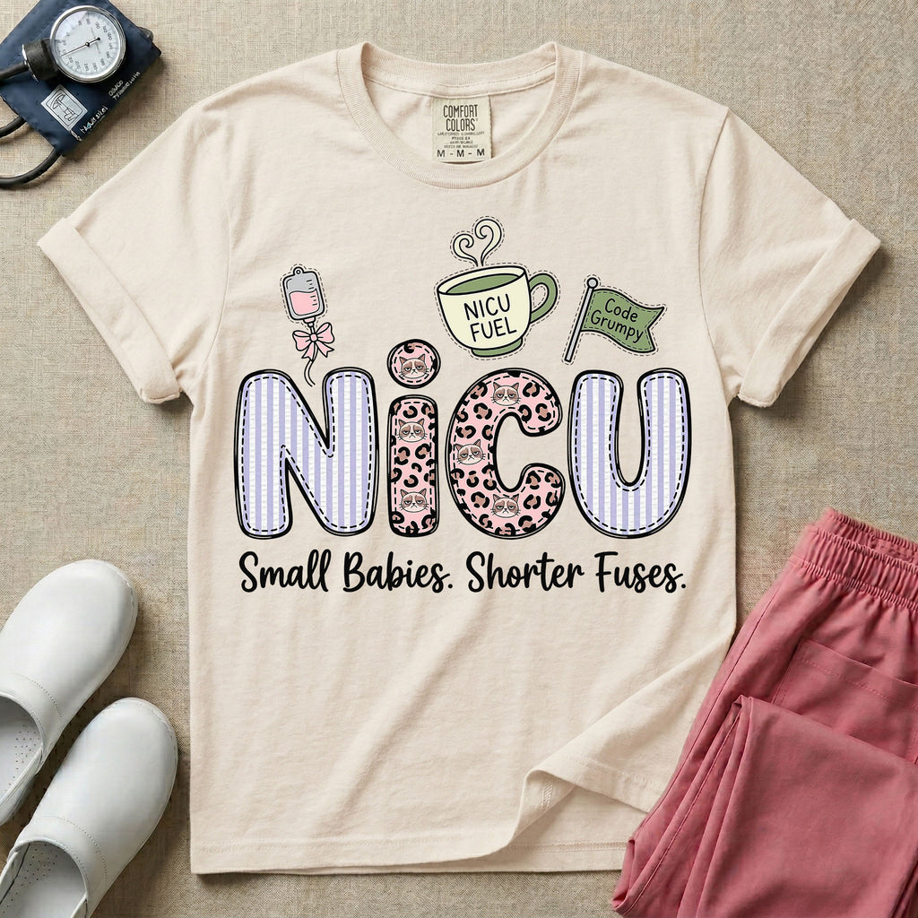 A funny t-shirt for NICU nurses featuring the large text "NICU" patterned with purple stripes and pink leopard print containing grumpy cat faces, accompanied by graphics of an IV bag with a pink bow, a steaming coffee cup reading "NICU FUEL", a green flag saying "Code Grumpy", and the bottom text "Small Babies. Shorter Fuses."