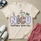 A funny t-shirt for NICU nurses featuring the large text "NICU" patterned with purple stripes and pink leopard print containing grumpy cat faces, accompanied by graphics of an IV bag with a pink bow, a steaming coffee cup reading "NICU FUEL", a green flag saying "Code Grumpy", and the bottom text "Small Babies. Shorter Fuses."