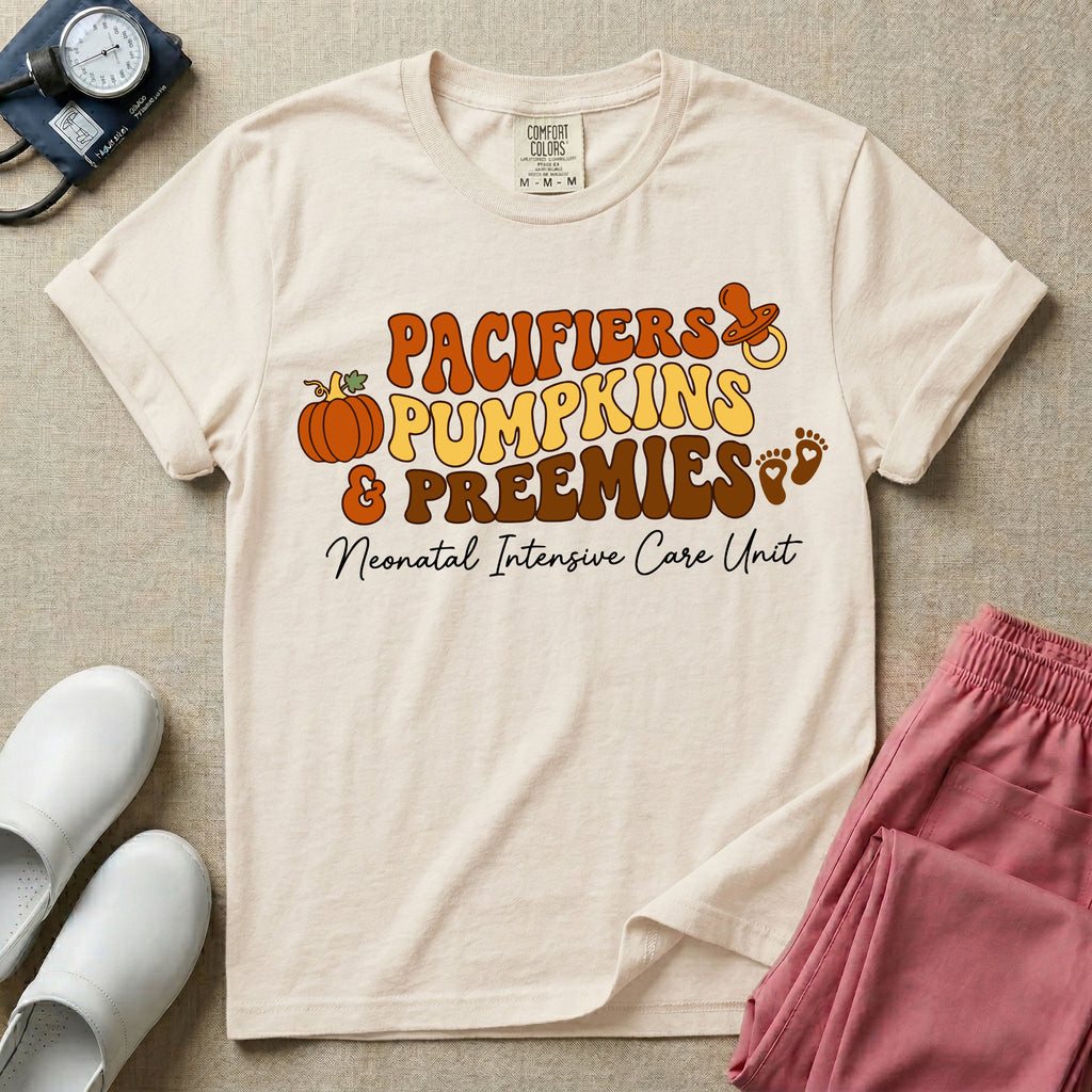 A t-shirt featuring the stacked text PACIFIERS PUMPKINS & PREEMIES in wavy orange, yellow, and brown retro lettering decorated with a pumpkin, pacifier, and baby footprints, with Neonatal Intensive Care Unit written in cursive below.