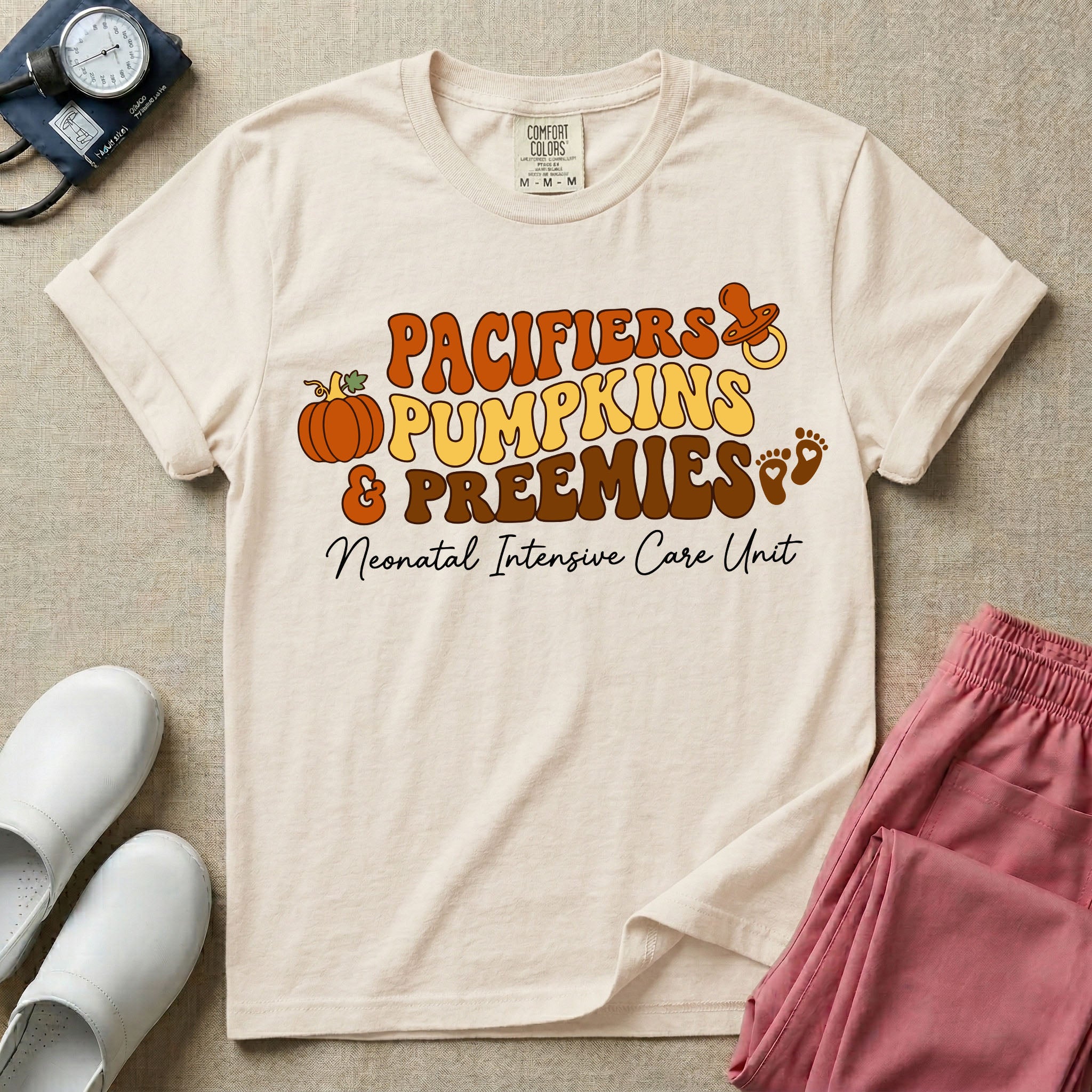 A t-shirt featuring the stacked text PACIFIERS PUMPKINS & PREEMIES in wavy orange, yellow, and brown retro lettering decorated with a pumpkin, pacifier, and baby footprints, with Neonatal Intensive Care Unit written in cursive below.