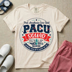 A t-shirt featuring a circular badge design with the text PACU SQUAD in block letters, medical icons like a heart monitor and stethoscope, and the phrase Waking You Up Is What We Do.