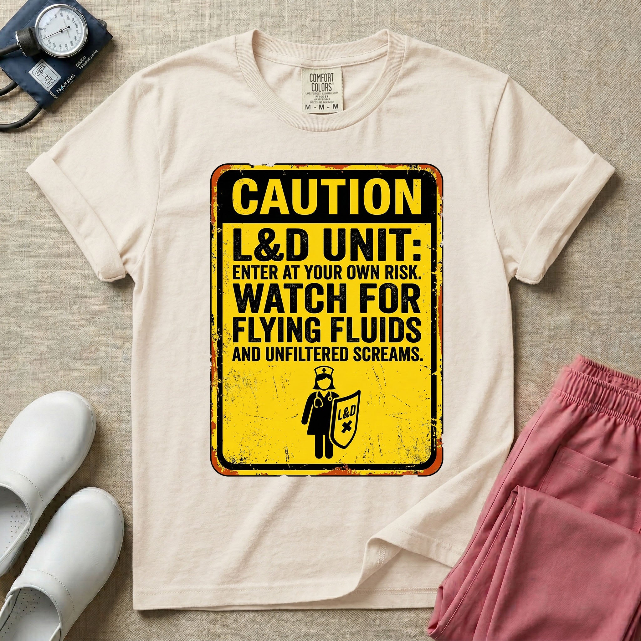 A humorous graphic tee for labor and delivery nurses featuring a distressed caution sign design with the text "CAUTION L&D UNIT: ENTER AT YOUR OWN RISK. WATCH FOR FLYING FLUIDS AND UNFILTERED SCREAMS." above a stick figure nurse holding a shield.