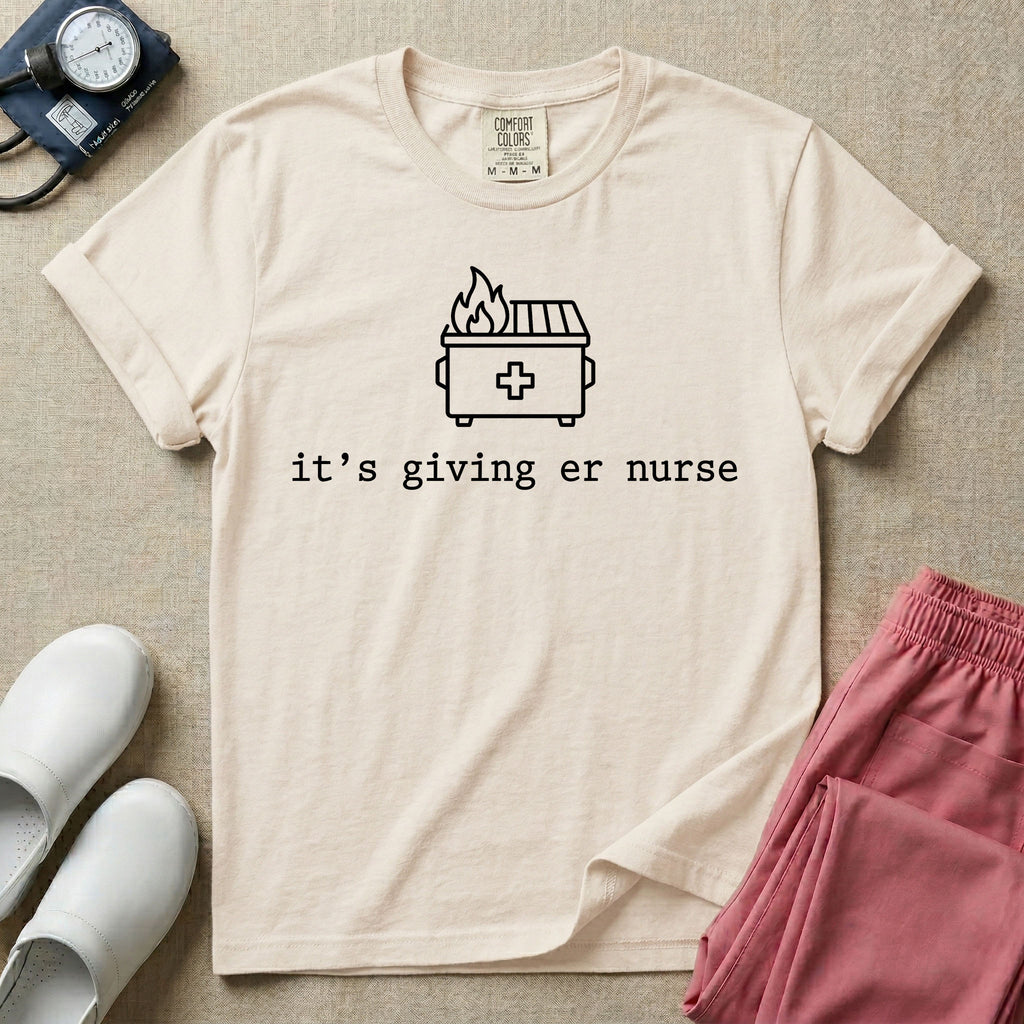 A funny minimalist ER nursing t-shirt featuring a simple white line drawing of a dumpster on fire with a medical cross on it, sitting above the lower-case typewriter text "it's giving er nurse".