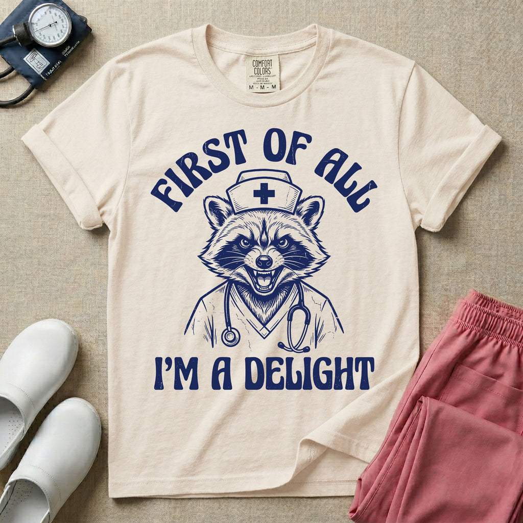 A humorous graphic of a raccoon dressed in a nursing cap and scrub jacket with a stethoscope, with the text "FIRST OF ALL I'M A DELIGHT", in ivory color.