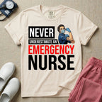 A retro ER nursing t-shirt featuring the bold text "NEVER UNDERESTIMATE AN EMERGENCY NURSE" alongside a vintage graphic of a masked nurse flexing her arm in a classic Rosie the Riveter pose