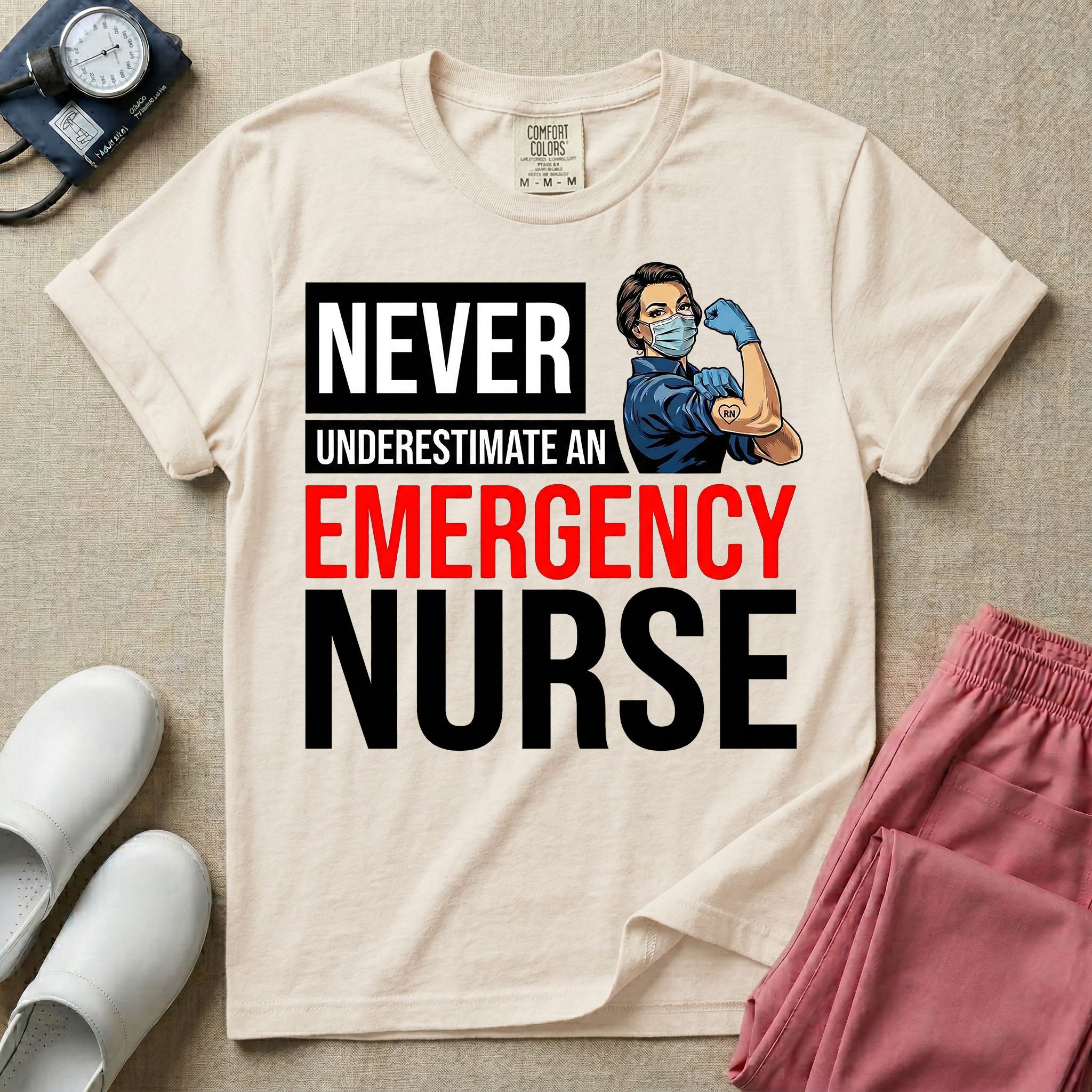 A retro ER nursing t-shirt featuring the bold text "NEVER UNDERESTIMATE AN EMERGENCY NURSE" alongside a vintage graphic of a masked nurse flexing her arm in a classic Rosie the Riveter pose
