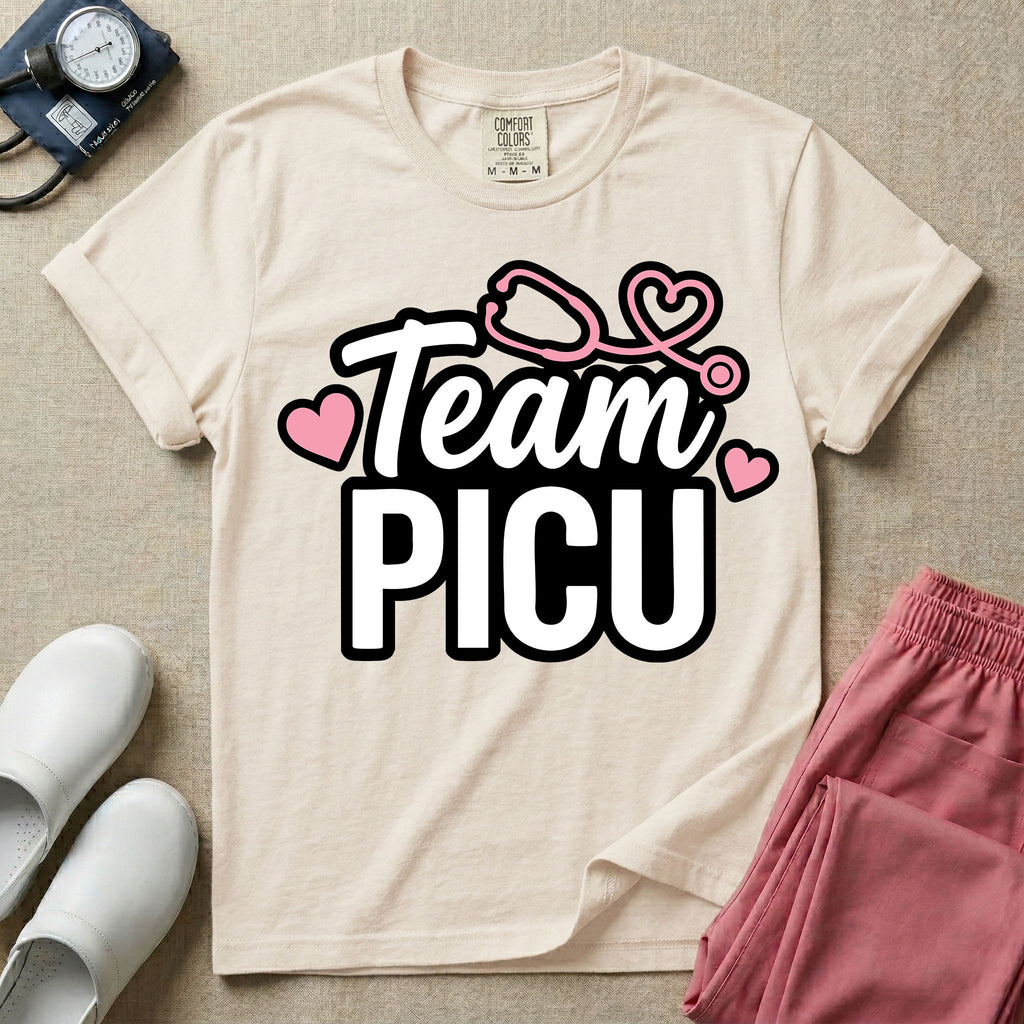 A descriptive graphic tee for pediatric intensive care nurses featuring the text "Team PICU" in bold white lettering, accented with pink hearts and a pink stethoscope design.