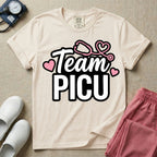 A descriptive graphic tee for pediatric intensive care nurses featuring the text "Team PICU" in bold white lettering, accented with pink hearts and a pink stethoscope design.
