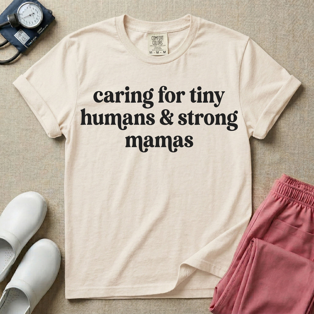 A minimalist nursing t-shirt featuring the text "caring for tiny humans & strong mamas" written in a retro white serif font.
