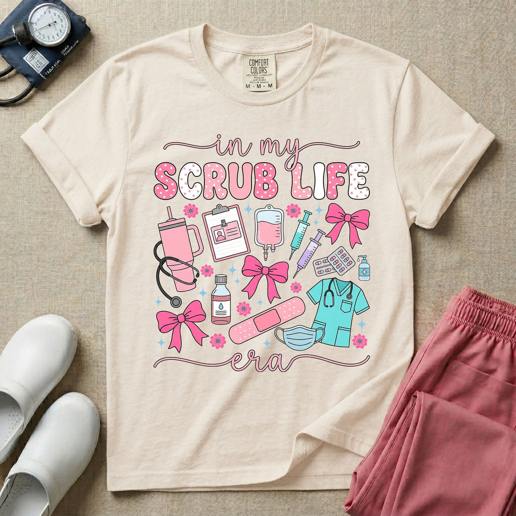 A cute general nursing t-shirt featuring the retro text "in my SCRUB LIFE era" surrounded by coquette medical graphics including a pink tumbler cup, stethoscope, IV bag with pink bows, clipboard, and blue scrubs.