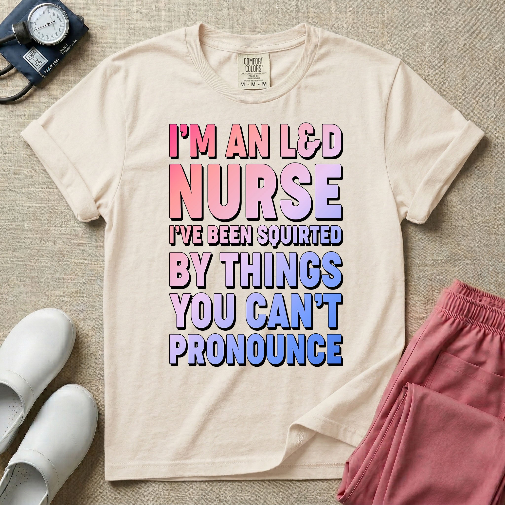 A humorous graphic tee for labor and delivery nurses featuring bold, gradient block lettering that reads "I'M AN L&D NURSE I'VE BEEN SQUIRTED BY THINGS YOU CAN'T PRONOUNCE".