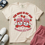 A t-shirt featuring two jars of strawberry jam surrounded by small hearts and strawberries with the text THE NICU IS MY JAM arched above and Neonatal ICU Nurse written in a retro script below.