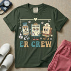 A retro-style t-shirt for emergency room nurses featuring the text "ER CREW" below a vintage cartoon illustration of a medicine bottle, a grumpy clipboard holding an AMA form, and a sandwich wearing a nurse cap walking together.
