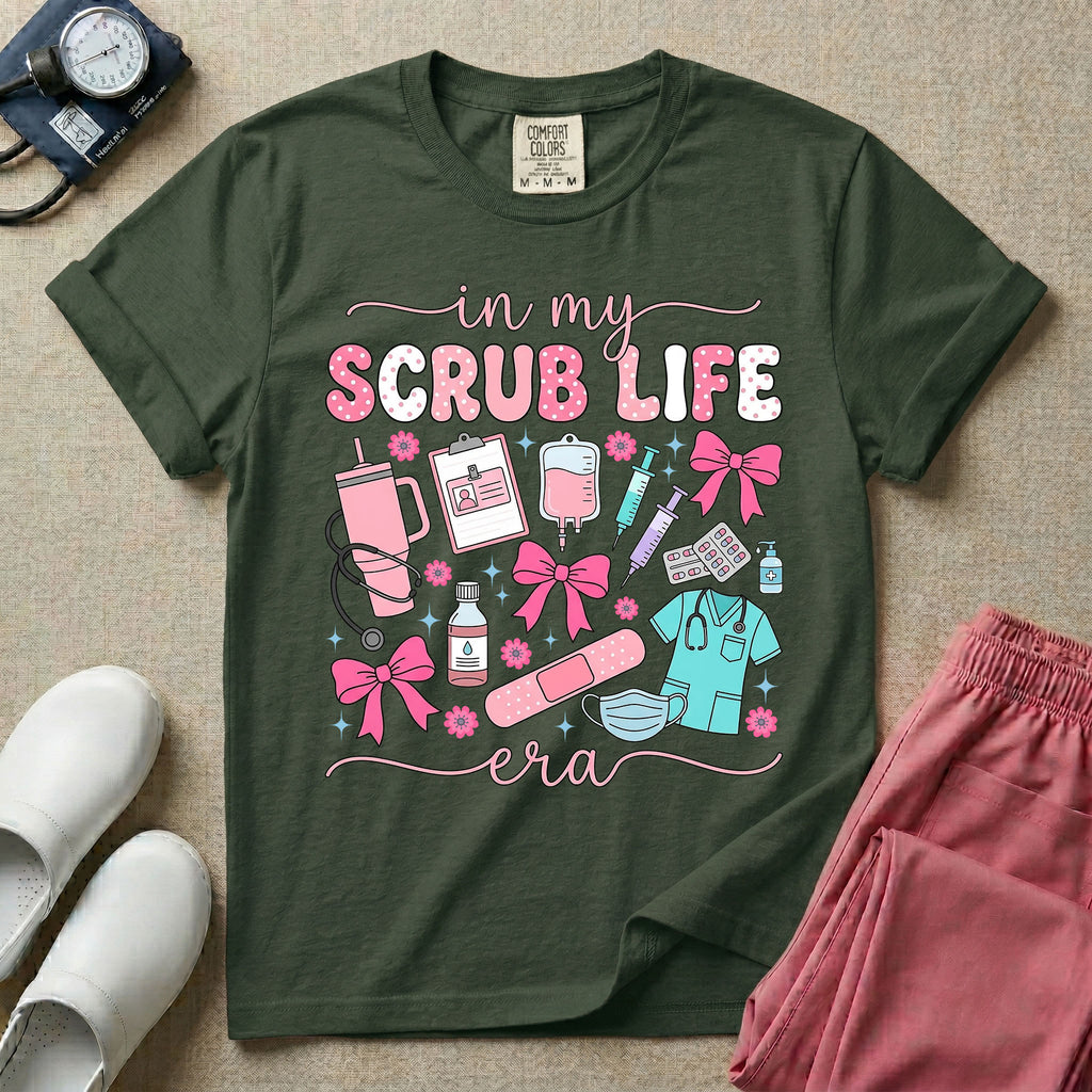 A cute general nursing t-shirt featuring the retro text "in my SCRUB LIFE era" surrounded by coquette medical graphics including a pink tumbler cup, stethoscope, IV bag with pink bows, clipboard, and blue scrubs.