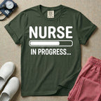 General nursing student t-shirt featuring a white loading bar graphic and the text "NURSE IN PROGRESS..." on a dark gray garment, in moss color.