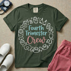 A postpartum nursing t-shirt featuring the stacked text "Fourth Trimester Crew" in blue and pink retro fonts, surrounded by a circular border of white minimalist line drawings depicting newborn and postpartum care items including a breast pump, swaddled baby, maternity bra, maxi pad, stethoscope, wipes, and a nursing pillow.