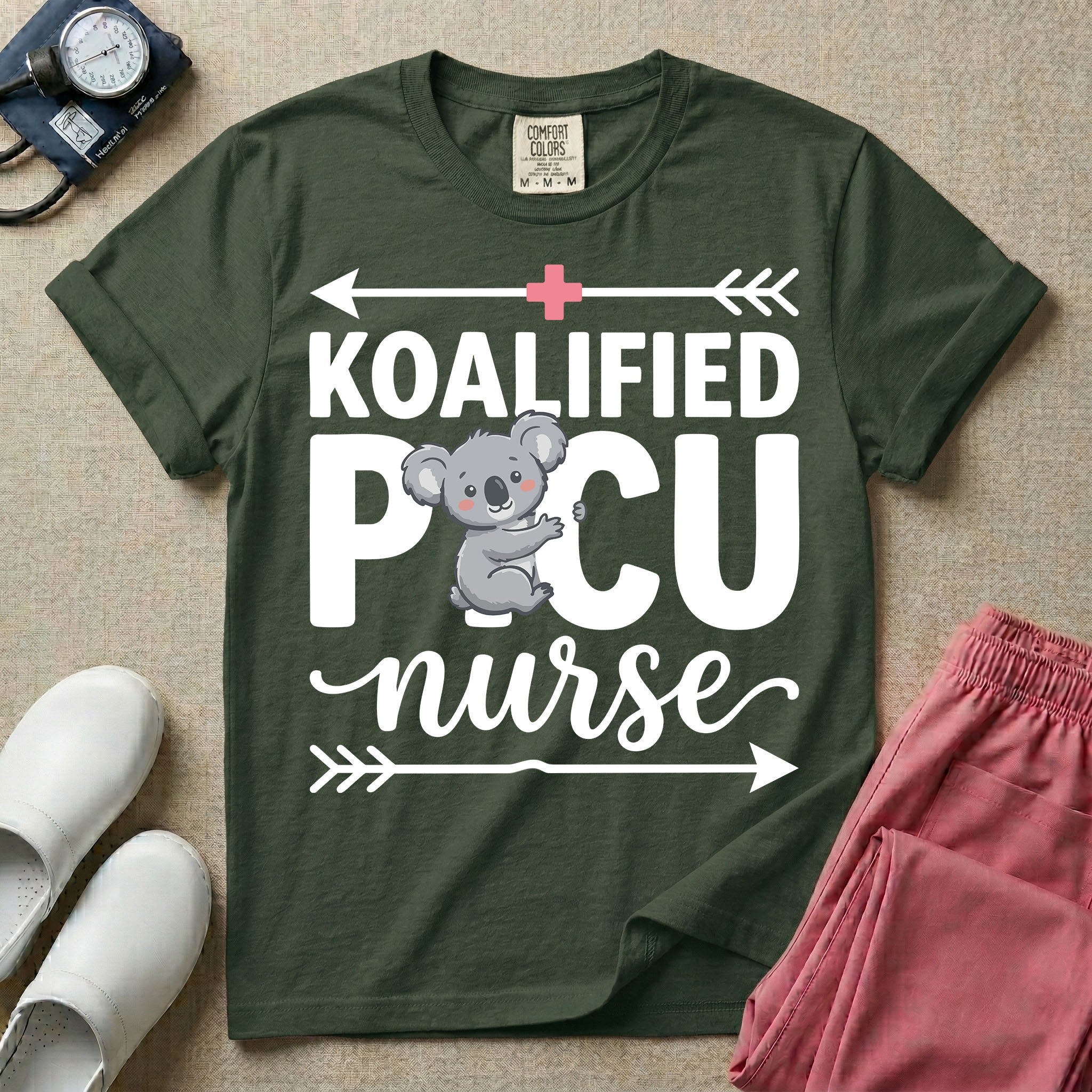 A funny pediatric intensive care nursing t-shirt featuring the pun text "KOALIFIED PICU nurse" with a cute koala graphic replacing the letter I in PICU, framed by decorative arrows and a pink medical cross.