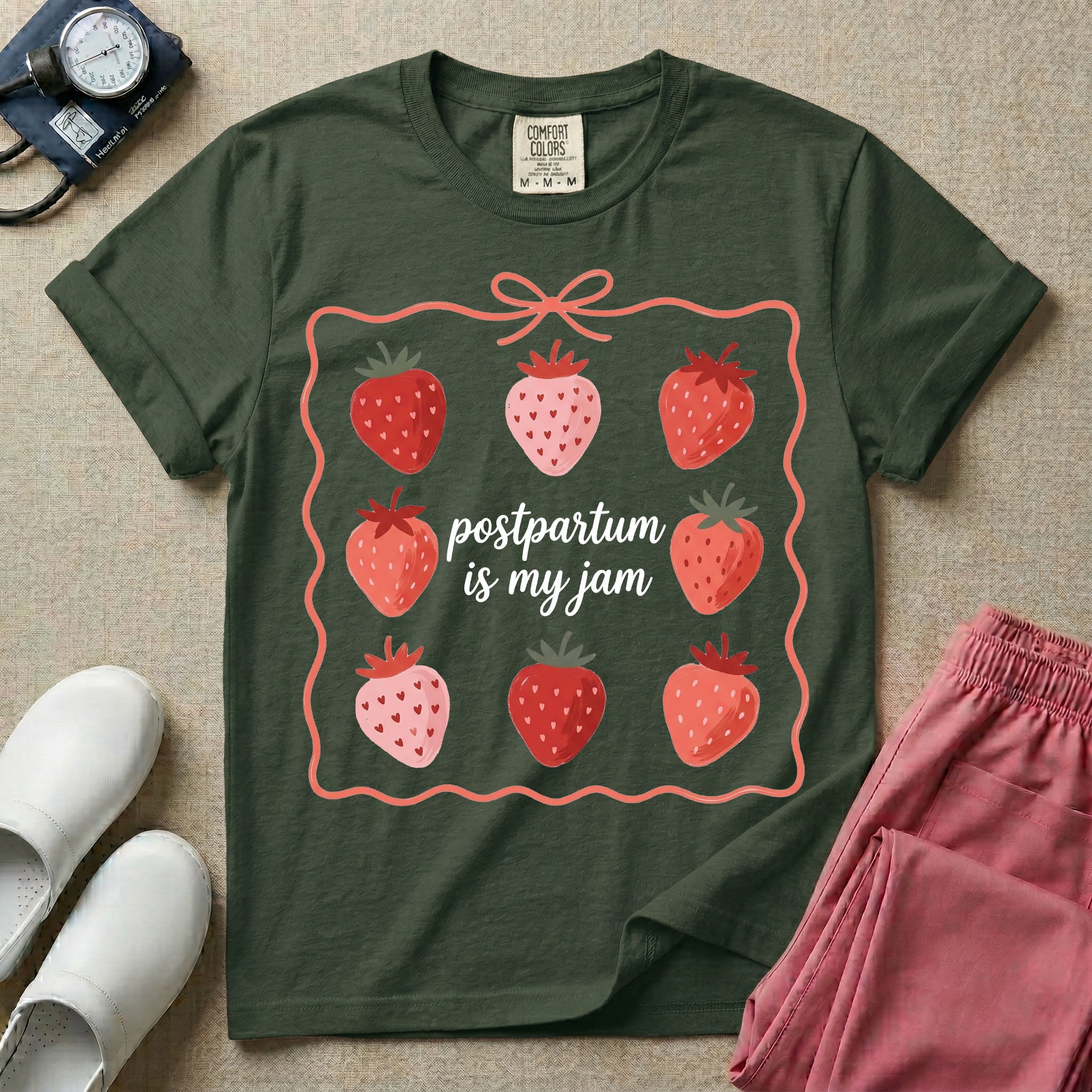 A funny and cute postpartum nursing t-shirt featuring the pun text "postpartum is my jam" surrounded by a graphic of red and pink strawberries, enclosed in a decorative wavy border with a bow at the top.