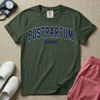 A t-shirt featuring the word POSTPARTUM arched in large collegiate block letters above the word NURSE in a smaller, matching font.