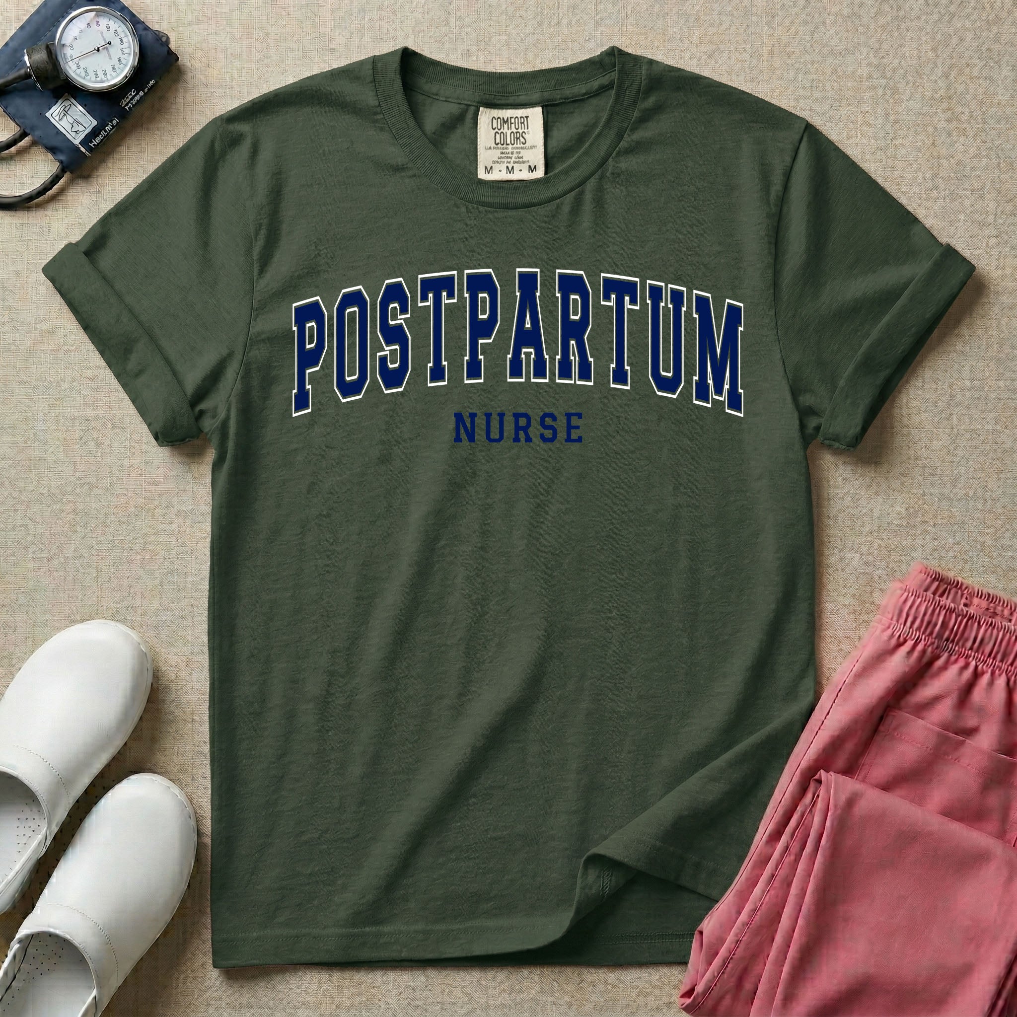 A t-shirt featuring the word POSTPARTUM arched in large collegiate block letters above the word NURSE in a smaller, matching font.