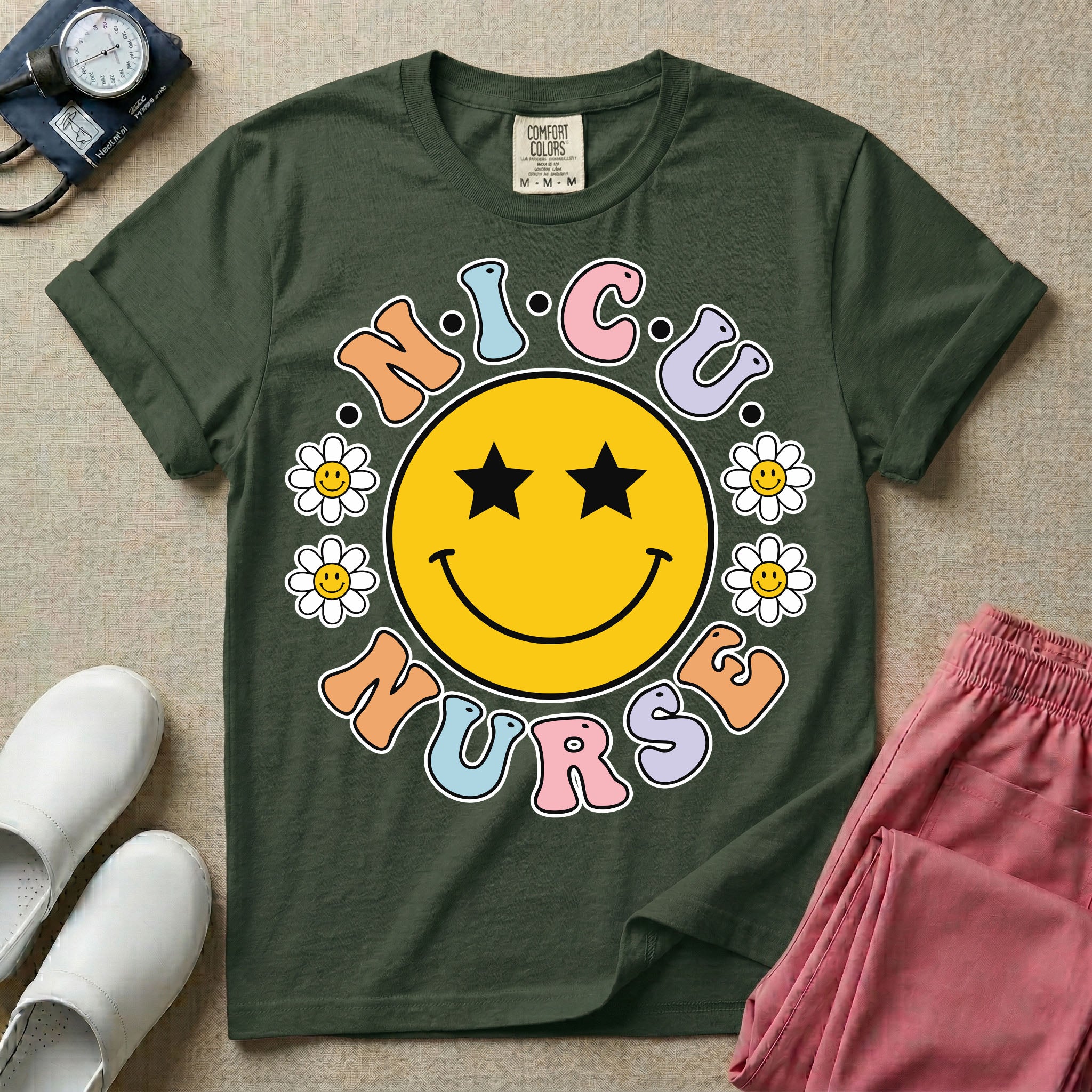 A t-shirt featuring a large yellow smiley face with star eyes surrounded by smiley face daisies and the text N.I.C.U. NURSE in pastel retro bubble lettering.